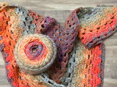 a multicolored crocheted scarf and ball of yarn on a wooden floor