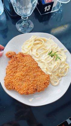 a white plate topped with pasta and sauce next to a chicken schnitz on a table