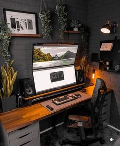 a computer desk with a monitor, keyboard and speakers on it in front of some potted plants