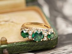 A wonderful statement piece, this vintage ring will elevate your outfits. The ring was made in 1967 and three green stones are the main part. The centre one is bigger than the side ones and they all have a unique dark green colour. In between then, four pearls make their appearance. The sides of the ring have repeated beautiful detail and its shank is a half round. Hallmarks: The ring is stamped 9, 375, and has the letter m for 1967. An engraving of love inside the shank, shows that the ring was Green Emerald Three-stone Birthstone Ring, Heirloom Green Birthstone Ring For May, Heirloom Green May Birthstone Ring, Vintage Hallmarked Emerald Jewelry, Vintage Gold Emerald Ring For Wedding, Vintage Gold Emerald Wedding Ring, Heirloom Green Emerald Ring For Wedding, Heirloom Green Emerald Ring With Three Stones, Heirloom Style Three Stone Green Emerald Ring