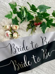 a bride to be sash laying on top of a bed next to flowers and greenery