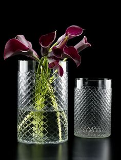 two glass vases with flowers in them on a black surface, one is empty