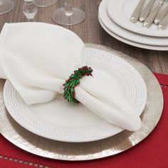 a white plate topped with a napkin next to silver and red place settings on a wooden table