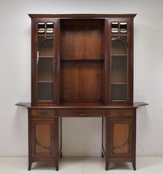 an old wooden desk with glass doors and shelves on the top, against a white brick wall