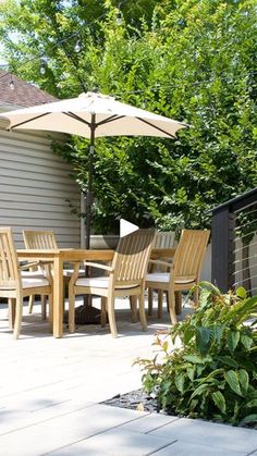 an outdoor dining table and chairs on a patio with umbrellas over the tables, surrounded by greenery