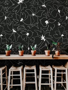 several potted plants sit on stools in front of a wall with black and white designs