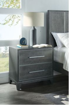 a nightstand with a book on top of it next to a lamp and bed in a room