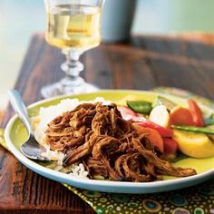 a plate with meat, rice and vegetables next to a glass of wine