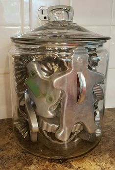 a glass jar filled with metal gears on top of a countertop next to a tile wall