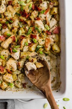 a casserole dish with chicken, vegetables and rice in it next to a wooden spoon