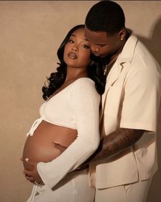 a pregnant woman standing next to a man in a white suit and tan shirt with tattoos on his arm