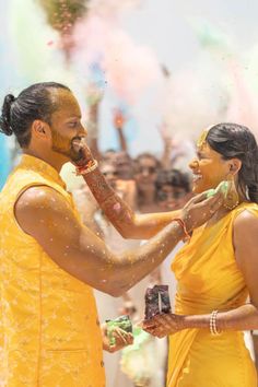 a man and woman standing next to each other with colored powder on their faces in front of them