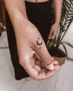 a person with a small crescent tattoo on their left hand, holding the finger of another person