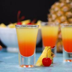 three glasses filled with different colored drinks on top of a blue tablecloth next to pineapples