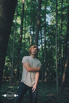 a young man standing in the middle of a forest