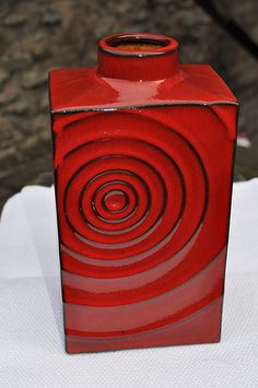 a red vase sitting on top of a white cloth