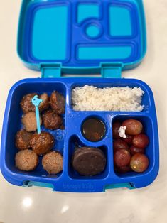 a blue lunch box filled with rice, meatballs and grapes next to other food items