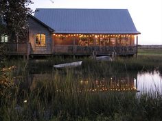 a boat sits on the water in front of a house with lights strung from it's windows