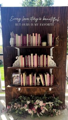 a book shelf with books on it and flowers in the foreground, next to a sign that says every love story is beautiful but ourss my favorite