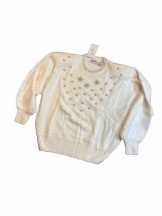 This exquisite Eddie Wassin sweater in size Medium features a crew neck and long sleeves. The sweater is made of soft angora material and is intricately knit with rhinestone accents. The pullover style sweater is perfect for the fall, winter, or spring seasons. The sweater also features pearls and shoulder pads for added style and comfort. The brand, Eddie Wassin, is known for producing high-quality clothing items and this sweater is no exception. Add this beautiful sweater to your wardrobe today! Winter Embellished Long Sleeve Tops, White Crew Neck Sweater For Parties, Embellished Long Sleeve Tops For Winter, Embellished Crew Neck Sweater For Fall, Cream Winter Party Top, Cream Party Tops For Winter, Elegant Crew Neck Sweater For Party, Winter Party Sweater With Crew Neck, Elegant Winter Tops With Rhinestones