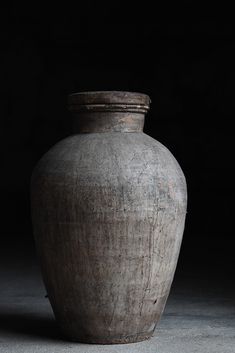 a large gray vase sitting on top of a cement floor next to a black wall