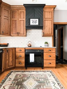 a kitchen with wooden cabinets and white tile backsplash, an area rug on the floor