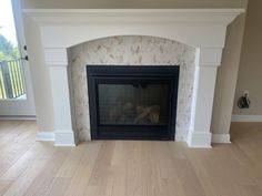 an empty living room with a fireplace and hardwood floors in the middle, looking out onto a balcony