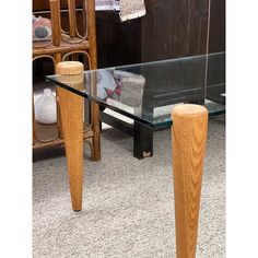 a glass table with two wooden legs in front of a book shelf and other furniture