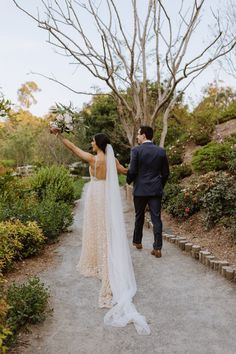 a bride and groom walking down a path holding their arms in the air as they look at each other