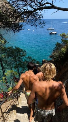 two men walking up some stairs towards the ocean with boats in the water behind them