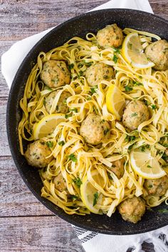 a skillet filled with pasta and meatballs on top of a wooden table next to a napkin