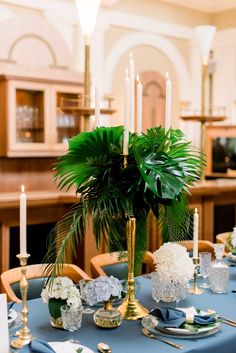 a blue table cloth with white flowers and greenery is set for a formal dinner