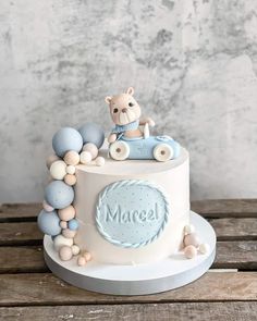 a small cake with a teddy bear on top and balloons around the edges that spell it's name