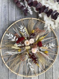 an arrangement of dried flowers in a wicker basket on a wooden table next to feathers