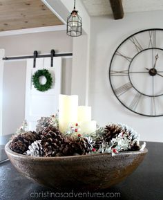 a bowl filled with pinecones and candles on top of a table next to a clock