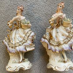 two porcelain figurines sitting next to each other on a carpeted floor in front of a wall