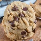 two chocolate chip cookies sitting on top of a wooden cutting board