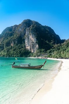 a boat is sitting on the beach in front of a mountain and clear blue water