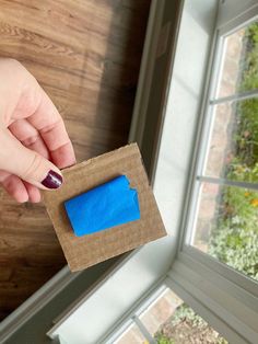 a person holding a piece of brown paper in front of a window with a blue sticker on it