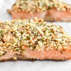 two salmon fillets with nuts and seasoning sitting on top of white parchment paper