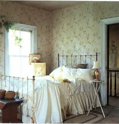 a white bed sitting in a bedroom next to a window with flowers on the wall