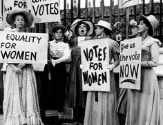 black and white photograph of women holding signs in front of gates with words on them