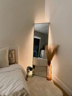 a bedroom with a bed, mirror and vase on the floor in front of it