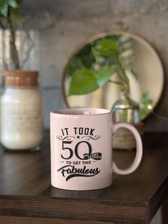 a pink coffee mug sitting on top of a wooden table next to a potted plant