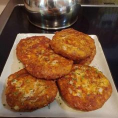 four crab cakes on a white plate next to a silver pot