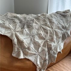 a white crocheted blanket sitting on top of a brown leather couch next to a window