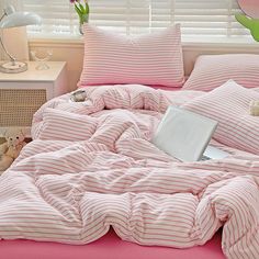 a bed with pink and white striped comforter next to a laptop computer on top of it