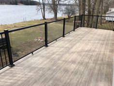 a wooden deck with black iron railings next to a lake