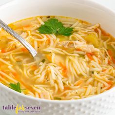 a white bowl filled with chicken noodle soup and garnished with parsley