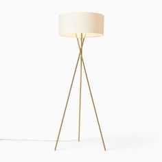 a floor lamp with a white shade on the top and a gold tripod base